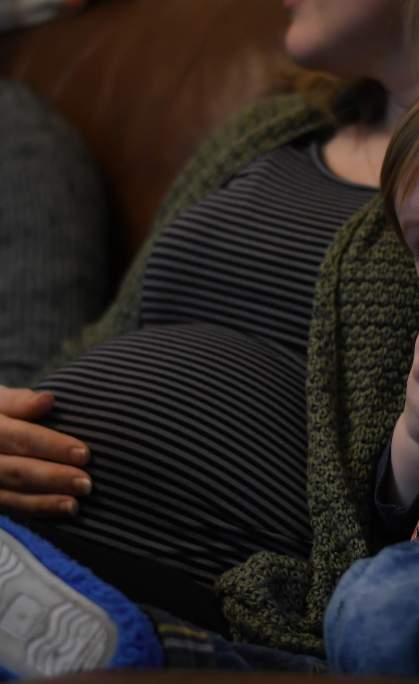 A woman, seated on a couch, cradles her pregnant stomach, reflecting a warm and affectionate bond between mother and child
