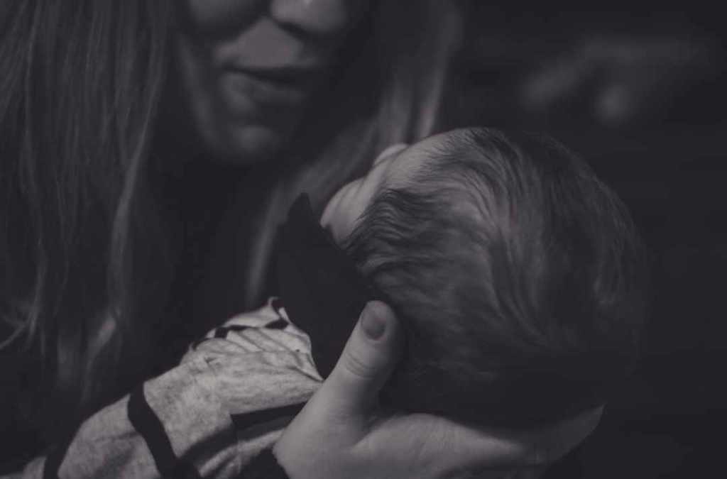 A monochrome image of a woman lovingly holding a baby in her arms, embodying warmth and nurturing in a serene and intimate setting.
