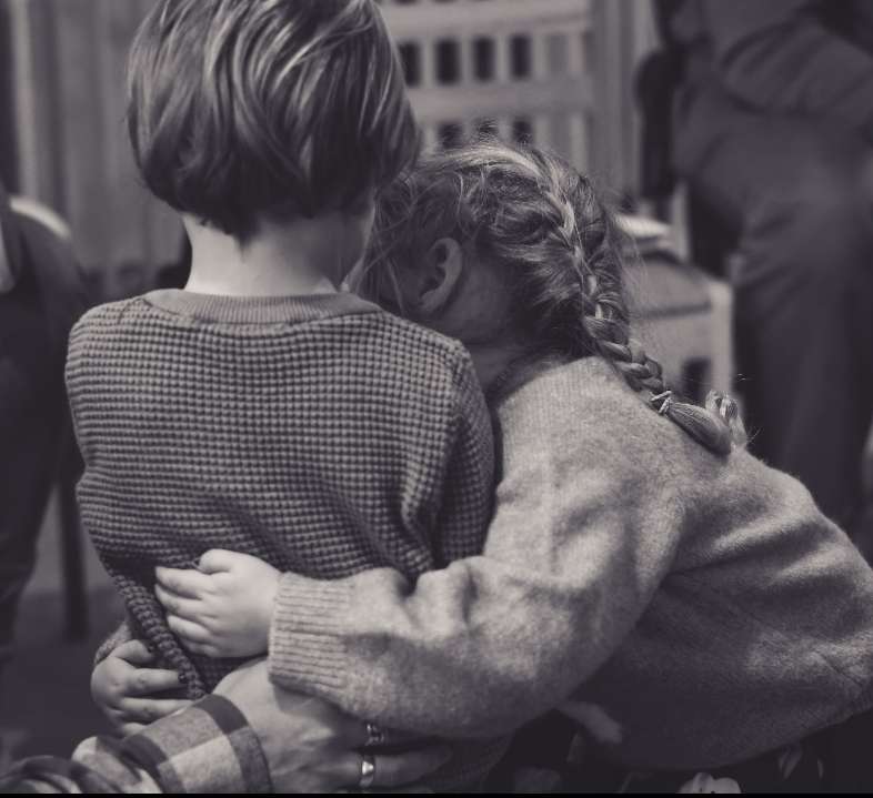 A black and white image capturing two children embracing each other in a moment of affection and warmth.